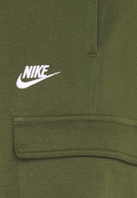 Olivgrön sweatshirt med en ficka, mjuk textur och vit broderad Nike-logotyp på vänster sida. Enkel design med rena linjer.