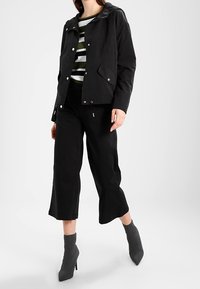 Black waterproof jacket with a hood, paired with a striped green and white top, black cropped pants, and gray ankle boots.