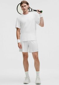 Conjunto atlético blanco que incluye una camiseta de manga corta y pantalones cortos a juego. Textura suave, tela liviana, con sutiles detalles acanalados y logotipo.