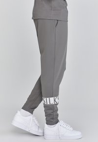 Grijze sportbroek met een slim fit, voorzien van een witte logoband bij de enkel. Gecombineerd met witte sneakers. Soepele textuur, casual ontwerp.