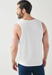 Top in cotone bianco senza maniche con scollatura rotonda, indossato da una persona di spalle, abbinato a pantaloni blue navy.