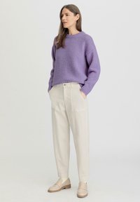 Violetti neulepaita, jossa on käännetty kaulus, yhdistetty vaaleisiin väljiin housuihin, joissa on etutaskut. Vaaleat loaferit, joissa on puunväriset pohjat.