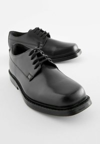 Chaussures habillées en cuir noir avec une texture lisse, bout arrondi et lacet à l'avant. Elles présentent un petit talon et des détails de couture discrets.