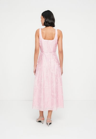 Robe rose avec un corsage ajusté et une jupe évasée, ornée de motifs floraux brodés. Fermeture éclair au dos, associée à des talons clairs.