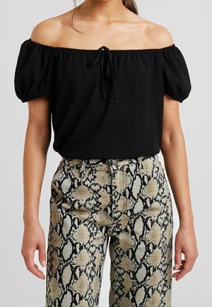 Woman wearing a black off-shoulder top with puff sleeves and high-waisted beige and black snake print pants.