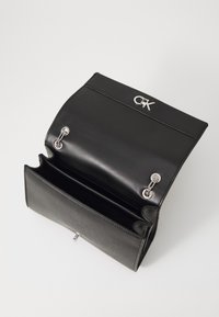 Borsa a tracolla in pelle nera con accessori in argento, logo sulla patta frontale, design aperto che rivela due scomparti e un interno testurizzato.