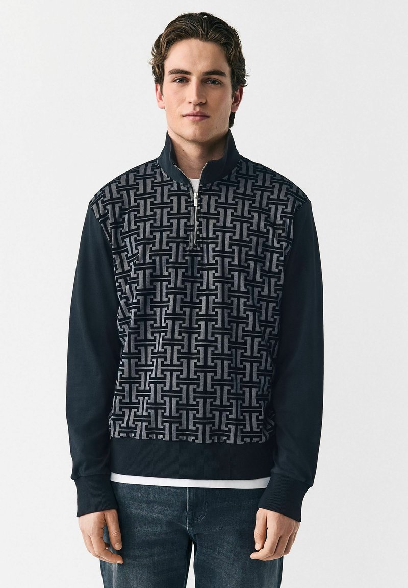 Sudadera con cremallera en negro y gris que presenta un patrón geométrico, textura suave, puños acanalados y un diseño de cuello alto.