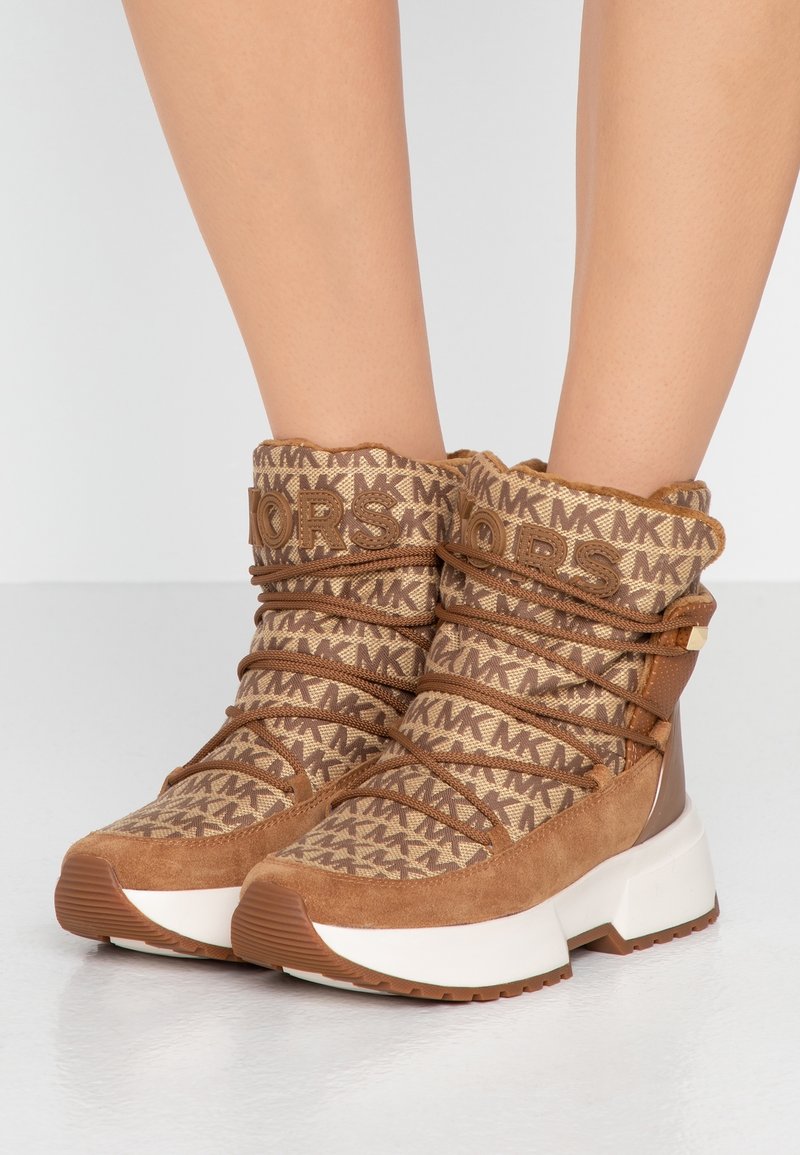 Bottines en textile marron avec un dessus en tissu à motifs, des accents en faux suède et des lacets élastiques, le tout reposant sur une semelle blanche épaisse.