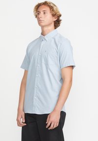 Chemise à manches courtes, bleu clair, avec un pocket poitrine et un motif subtil. Fabriquée en tissu lisse, avec un col classique.