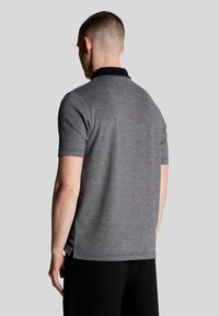 Grijze polo met korte mouwen en een marineblauwe kraag, voorzien van een gestructureerde stof en zijsplitten aan de zoom voor meer bewegingsvrijheid.