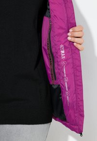 Lila wasserdichte Jacke mit Reißverschluss, ausgestattet mit Innenetiketten für wasserdicht, winddicht und atmungsaktiv Eigenschaften. Schwarze Fütterung sichtbar.