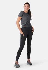Svarta leggings med sidofickor, kombinerade med en åtsittande grå T-shirt knuten i midjan. Modellen har på sig grå och orangea sneakers.