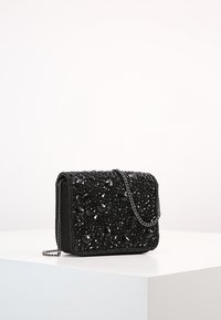 Borsa a tracolla nera con perline; presenta una superficie decorata con vari gemme nere e una forma rettangolare.