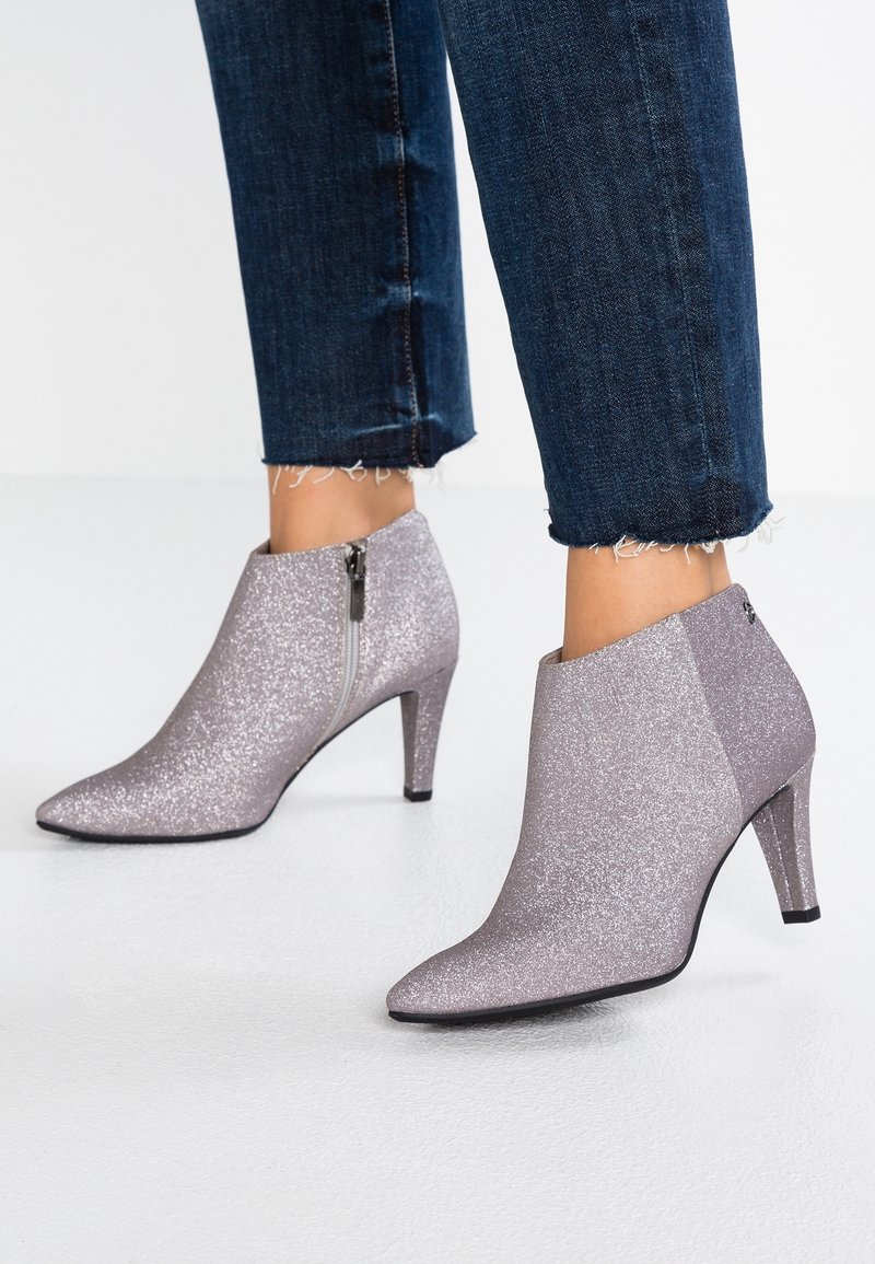Bottes lavande scintillantes montant à la cheville, avec fermetures éclair latérales et bouts pointus, portées avec un jean bleu foncé effiloché.