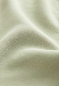 Tessuto verde chiaro, superficie liscia, motivo di tessitura sottile, drappeggiato per mostrare contorni morbidi e pieghe delicate.