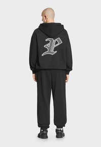 Czarny zestaw bluz i spodni dresowych, z wyraźnym białym logo na plecach, wykonany z miękkiego materiału o luźnym kroju.