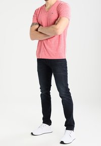 Červené vřesové tričko s výstřihem do V, tmavé džíny a bílé sportovní boty. Jednoduchý design, slim fit, s texturovanou látkou a minimálním brandováním.
