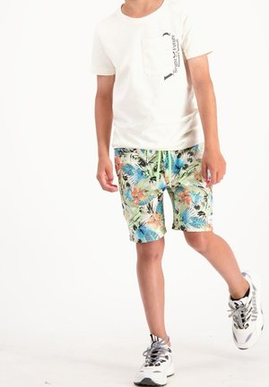 Chemise blanche à manches courtes avec une poche ; short imprimé avec motifs floraux verts ; baskets noires et blanches avec des lacets gris.