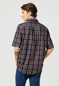 Korte mouw button-up shirt in marineblauw en bruin ruitpatroon, met een klassieke kraag en een ontspannen pasvorm, voorzien van een achterste schouderdetail.