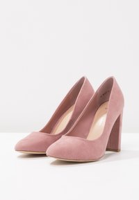Růžové semišové lodičky na vysokém podpatku s kulatou špičkou a robustním podpatkem. Hladká textura s minimalistickým designem, s mírně polstrovanou stélkou.