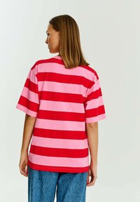 Červené a růžové pruhované tričko s krátkým rukávem, volného střihu, z měkké tkaniny a s kulatým výstřihem, kombinované s modrými džíny.