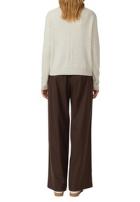 Kremowy sweter z dzianiny z prążkowanym dołem i długimi rękawami, w połączeniu z luźnymi brązowymi spodniami. Sweter ma detal w postaci środkowego szwu.