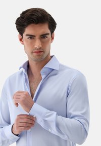 Hellblaues Hemd aus glattem Stoff mit tailliertem Schnitt, geknöpften Manschetten und klassischem Kragen.