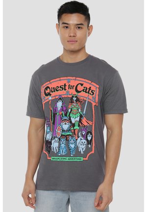 Man wearing gray shirt with colorful "Quest for Cats" fantasy roleplay design featuring characters and cats in armor with swords and staffs.