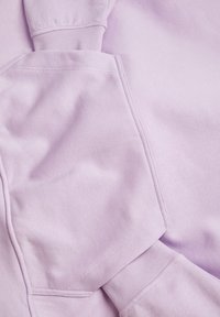 Lilla hettegenser med myk tekstur, ribbede mansjetter og synlige sømmer. Stoffet virker tykt og litt børstet.