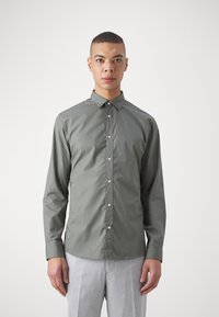 Camisa de botones de manga larga, color verde oliva, con cuello puntiagudo y botones blancos, hecha de una tela suave; estilo ajustado, con detalles de diseño mínimos.