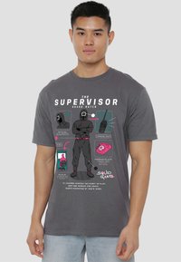 Gray short-sleeve t-shirt featuring a graphic print inspired by "Squid Game" with illustrated elements, text, and contrasting colors.