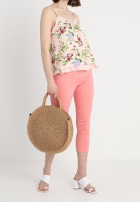 Top rosa con estampado floral y volantes, combinado con pantalones cortos coral. Accesorios incluyen un bolso redondo de mimbre y sandalias de tacón cuadrado blancas.