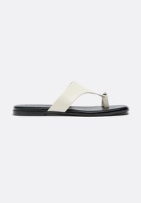 Sandale plate noire avec une large bride en cuir blanc et un anneau pour le gros orteil, design minimaliste, vue latérale sur un fond clair.