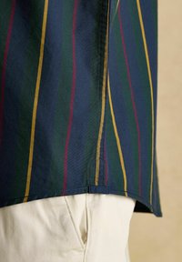 Detailný záber na tmavomodrú tkaninu s vertikálnymi zelenými, žltými a červenými pruhmi na krémových nohaviciach.