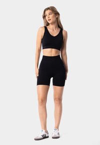 Black sports bra and high-waisted shorts made of stretchy material. The bra features a wide scoop neck; the shorts are fitted and thigh-length.