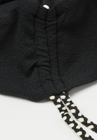 Tela de textura negra, fruncida en la parte superior con dos cordones trenzados. Los cordones tienen un patrón de colores alternos en negro y blanco.