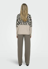Suéter beige con un patrón de cebra negro en la parte superior, combinado con pantalones de pierna ancha de color verde oliva. Mezcla de lana, ajuste casual, acabado texturizado.