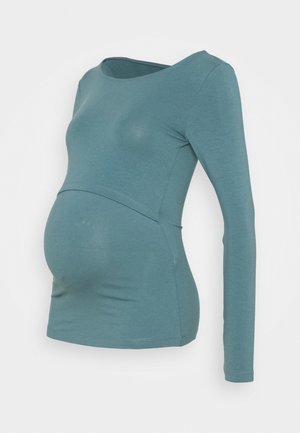 Modrý těhotenský top s dlouhým rukávem a vrstveným předním panelem navržený pro snadný přístup při kojení.