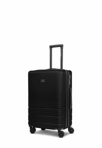 Valise rigide noire avec une surface texturée, un design à rainures verticales, une poignée rétractable et quatre roues multidirectionnelles.