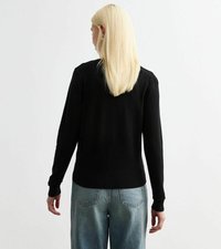 Maglione nero lavorato a maglia con maniche lunghe, polsini e orlo a costine. La parte posteriore presenta un colletto arrotondato. Abbinato a jeans in denim azzurro chiaro.