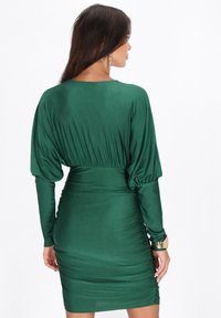 Rochie verde, ajustată, confecționată dintr-un material moale, cu mâneci lungi și puffate și o talie strânsă, având un design plisat pe spate.