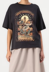 Sort bomulds t-shirt med korte ærmer, prydet med et grafisk tryk af en slange og sol i varme nuancer. Boxy fit med ribbet halsudskæring.