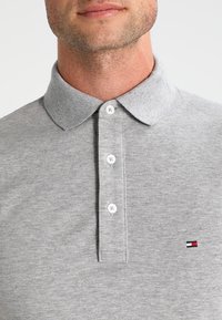 Polo grigio realizzato in tessuto testurizzato con colletto e patta con tre bottoni. Presenta un piccolo logo ricamato sul petto.