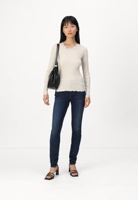 Beige bordázott hosszú ujjú felső fodros kivágással, sötétkék slim-fit farmerral, fekete válltáskával és magassarkú szandállal párosítva.