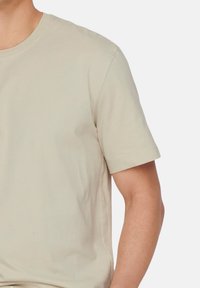 Beige Baumwoll-T-Shirt mit kurzen Ärmeln, Rundhalsausschnitt und glatter Textur, mit einer taillierten Silhouette und minimalen Nähten.