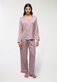 Set di pigiama in satin rosa chiaro con rifiniture bianche. Comprende una camicia con bottoni, una tasca e maniche lunghe, abbinata a pantaloni coordinati.