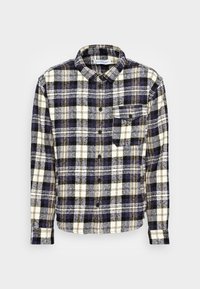 Rutig skjorta med knapp i marinblått, vitt och gult. Har en klassisk krage, långa ärmar och en ficka på bröstet. Mjuk tygstruktur.