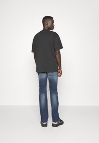 Μαύρη κοντομάνικη μπλούζα, από βαμβακερό ύφασμα, άνετη εφαρμογή, συνδυασμένη με μπλε τζιν παντελόνι. Μινιμαλιστικός σχεδιασμός με λαιμόκοψη τύπου crew.