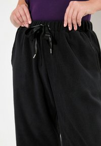 Zwarte fleece joggingbroeken met een zachte textuur, voorzien van een elastische tailleband en een zwarte satijnen koord met zilveren aglets.