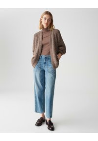Cardigan texturizzato marrone chiaro, dolcevita marrone e jeans a vita alta blu chiaro abbinati a mocassini scuri. Abbigliamento semplice e casual.